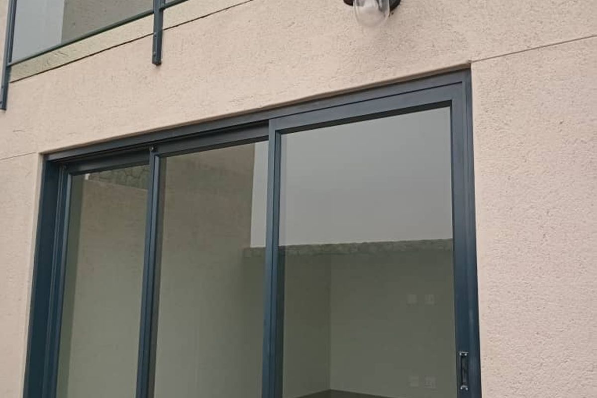 A view of a modern townhouse exterior featuring a glass balcony railing, sliding glass doors, and an outdoor wall-mounted light fixture.