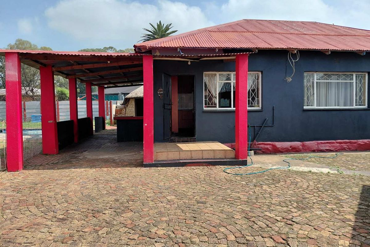 Rear view of the house featuring a covered patio area, corrugated metal roofing, and extensive brick paving in the yard.