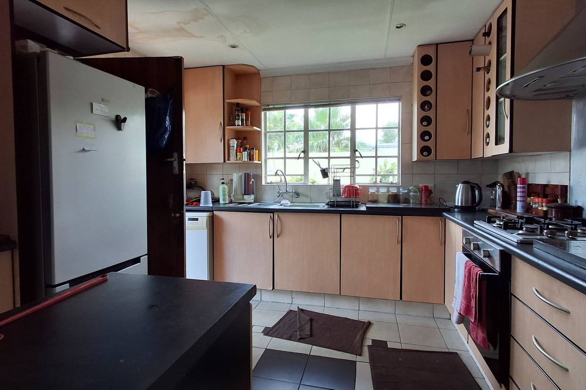 A dated kitchen featuring light wood-tone cabinetry, dark countertops, a built-in gas hob, and an integrated oven, with visible ceiling water damage.