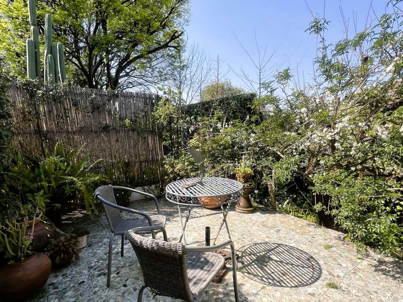 A private outdoor patio area featuring stone paving, surrounded by established garden greenery and a bamboo privacy screen.