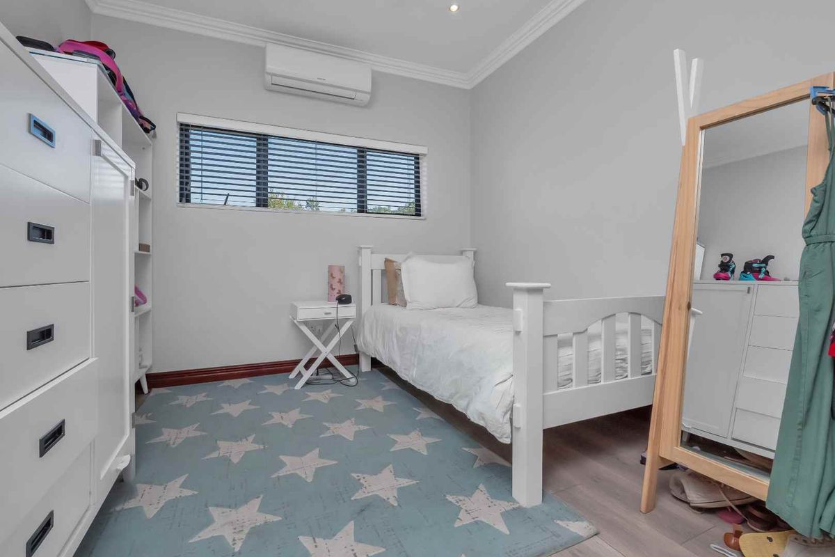 A well-maintained bedroom featuring light-toned laminate flooring, crown molding, and a wall-mounted air conditioning unit.