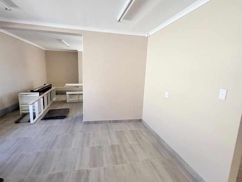 A bright, open-plan office space featuring neutral wall finishes, modern tiled flooring, and functional strip lighting, ready for professional fit-out.