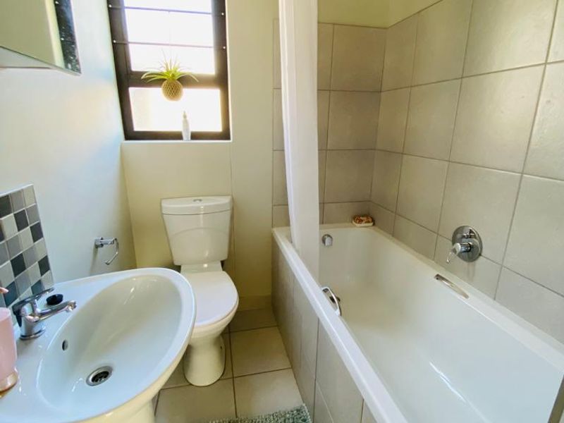 A functional bathroom featuring a pedestal basin, toilet, and a bathtub with a shower head, finished with neutral wall and floor tiles.