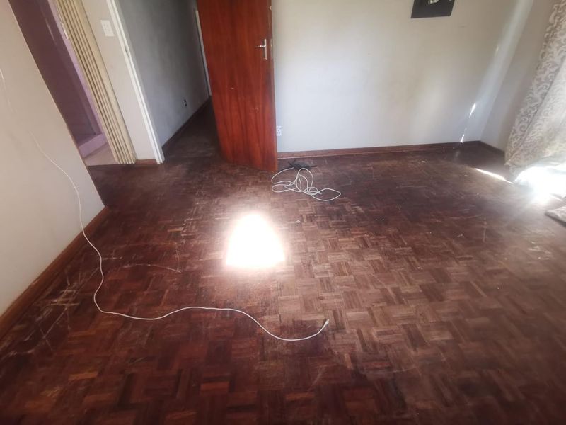 An empty bedroom featuring original parquet flooring and timber doors, requiring refinishing to restore its aesthetic appeal.