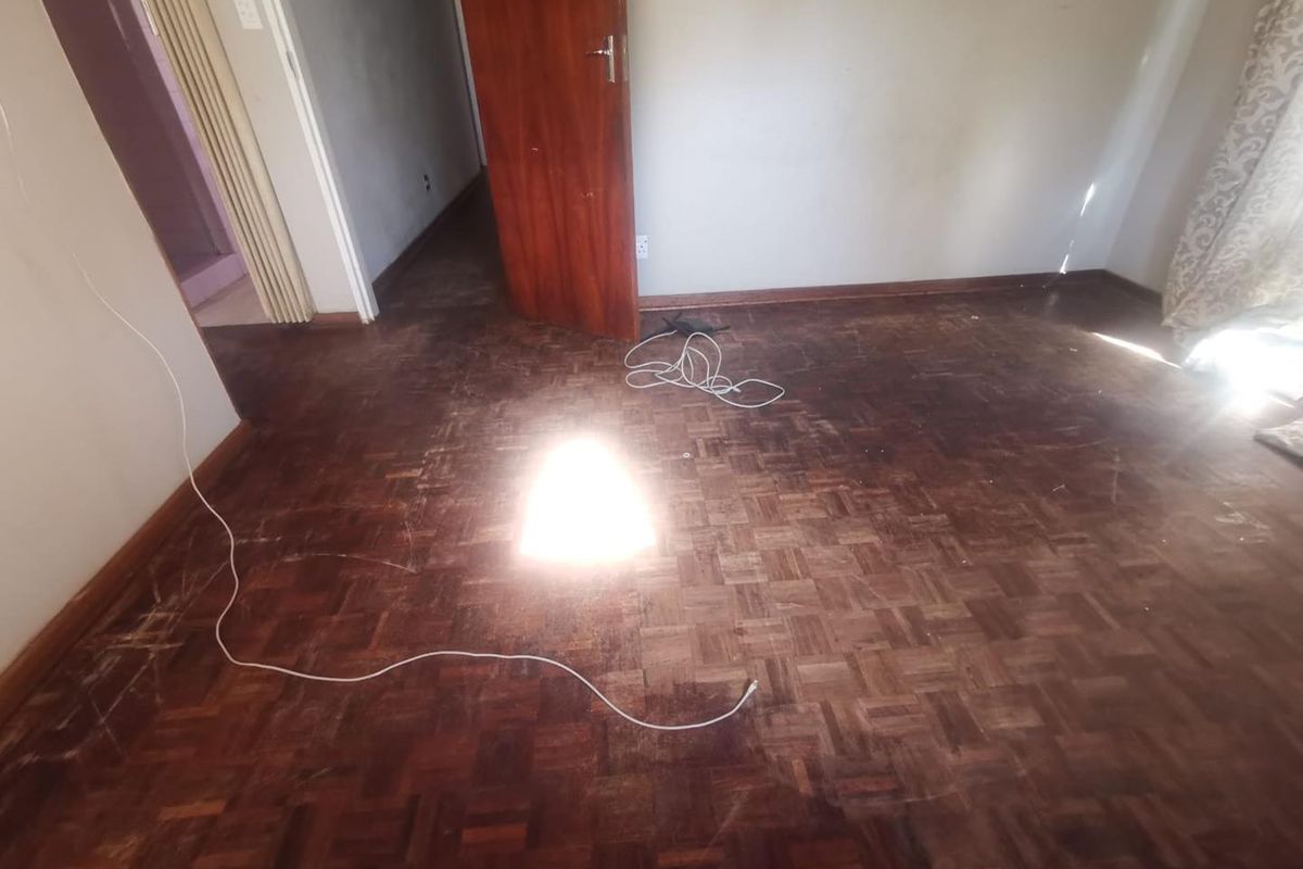 An empty bedroom featuring original parquet flooring and timber doors, requiring refinishing to restore its aesthetic appeal.