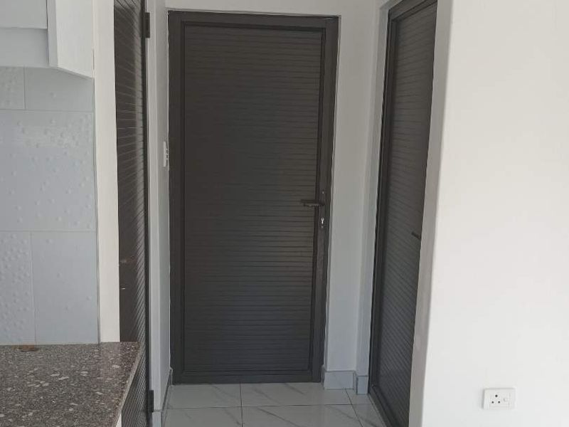 A clean, modern hallway featuring white tiled floors, dark louvered doors, and a granite countertop section, presenting a well-maintained and neutral interior space.