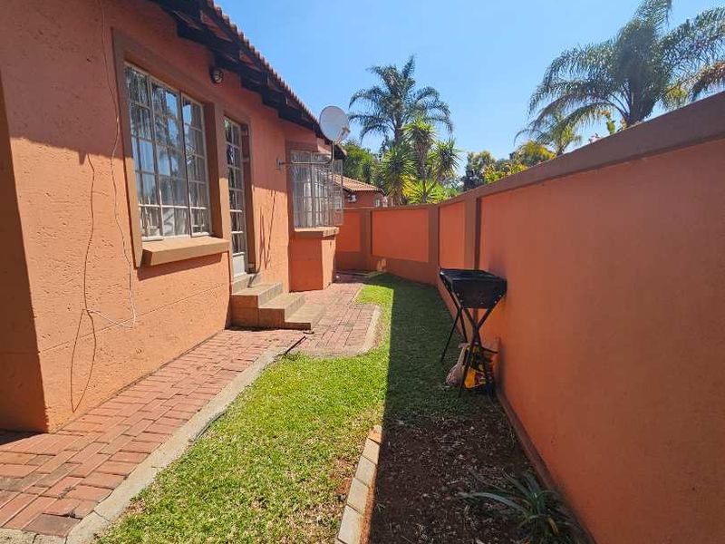 A side garden area featuring brick paving, a lawn, and a high boundary wall, providing a private outdoor space along the side of the house.