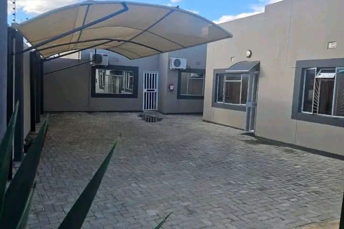 A paved rear courtyard area featuring a shade sail, external air conditioning units, and secure perimeter fencing.