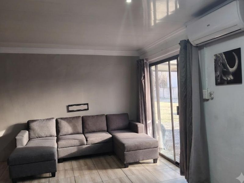 A comfortable living room featuring tiled flooring, cove molding, and a split-system air conditioner, with direct access to the outdoor area via sliding glass doors.