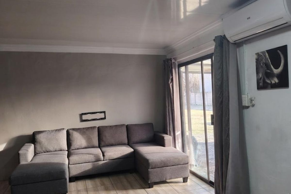 A comfortable living room featuring tiled flooring, cove molding, and a split-system air conditioner, with direct access to the outdoor area via sliding glass doors.