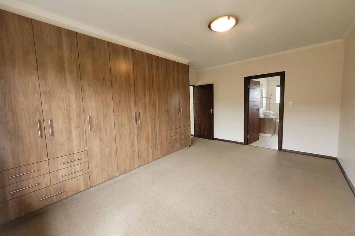 Spacious bedroom featuring extensive built-in wooden cabinetry and an en-suite bathroom with neutral carpeting and clean finishes.