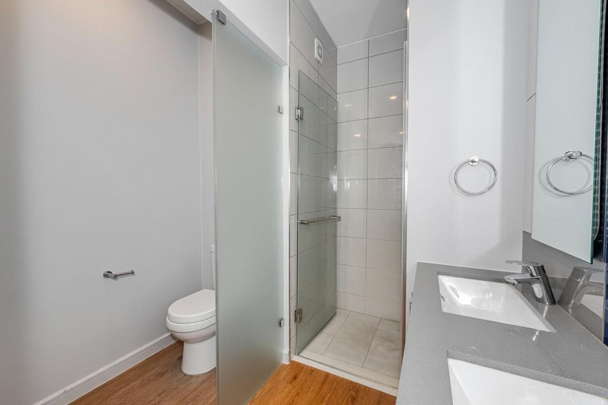 Modern bathroom featuring a double vanity with stone countertop, a glass-enclosed shower with tiled walls, and a separate toilet area with frosted glass partition.
