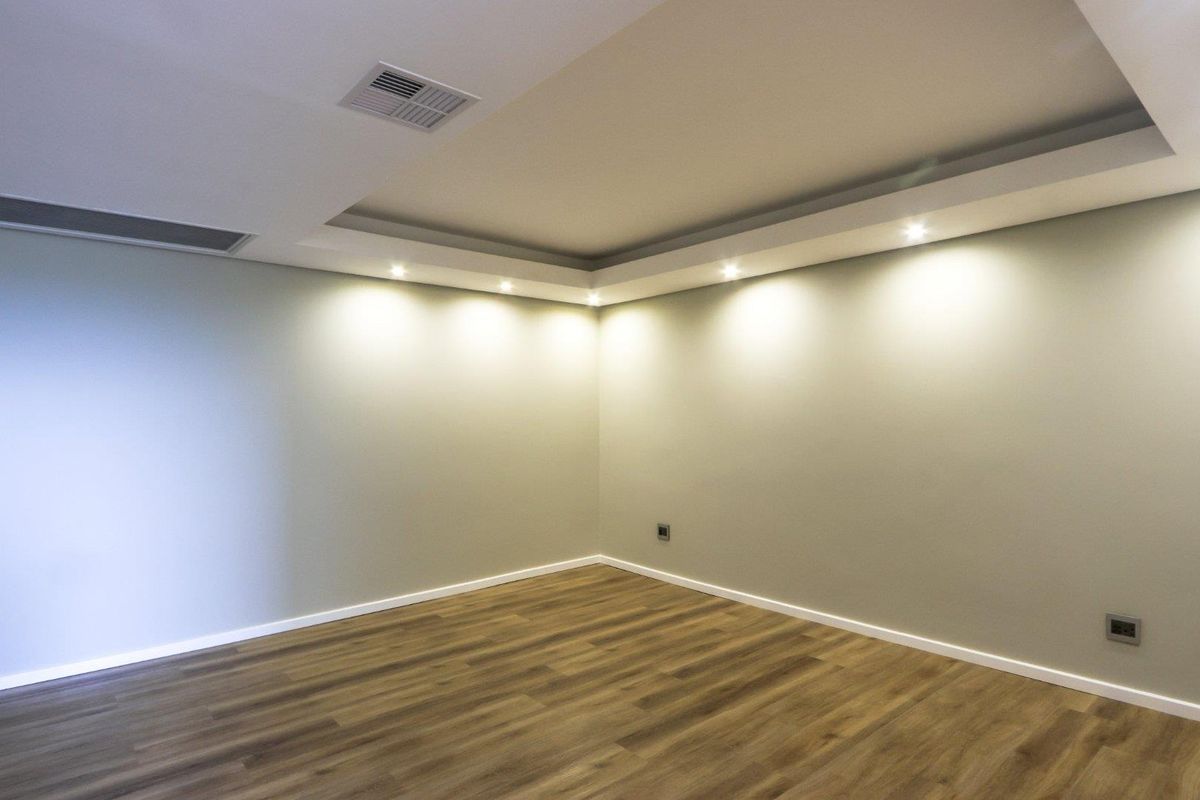 A bright, empty living space featuring modern laminate flooring, a stylish dropped ceiling bulkhead with recessed lighting, and integrated air conditioning.