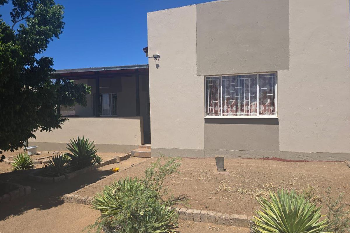 Exterior view of the house featuring a covered patio area, security bars on windows, and a low-maintenance garden with established shrubs.