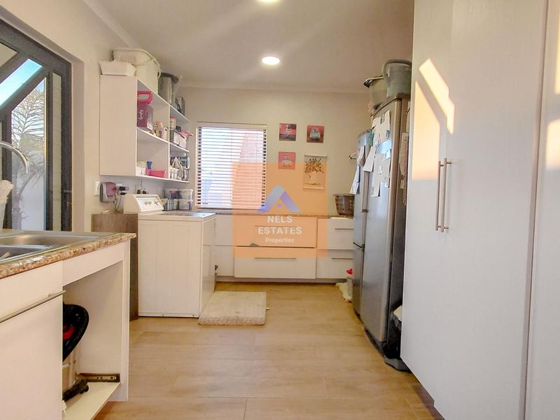 A functional laundry room featuring built-in cabinetry, granite countertops, a stainless steel sink, and tiled flooring with ample storage space.
