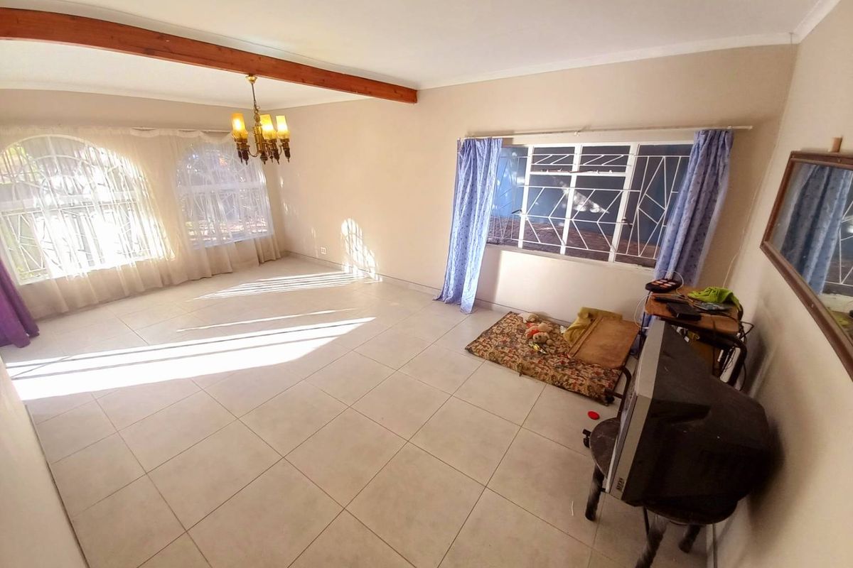 Spacious living area featuring large windows with security bars, tiled flooring, and a decorative exposed timber ceiling beam.