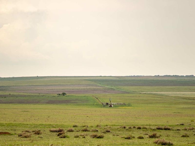 Expansive view of open farm land featuring a traditional wind pump and perimeter fencing across the rolling landscape.