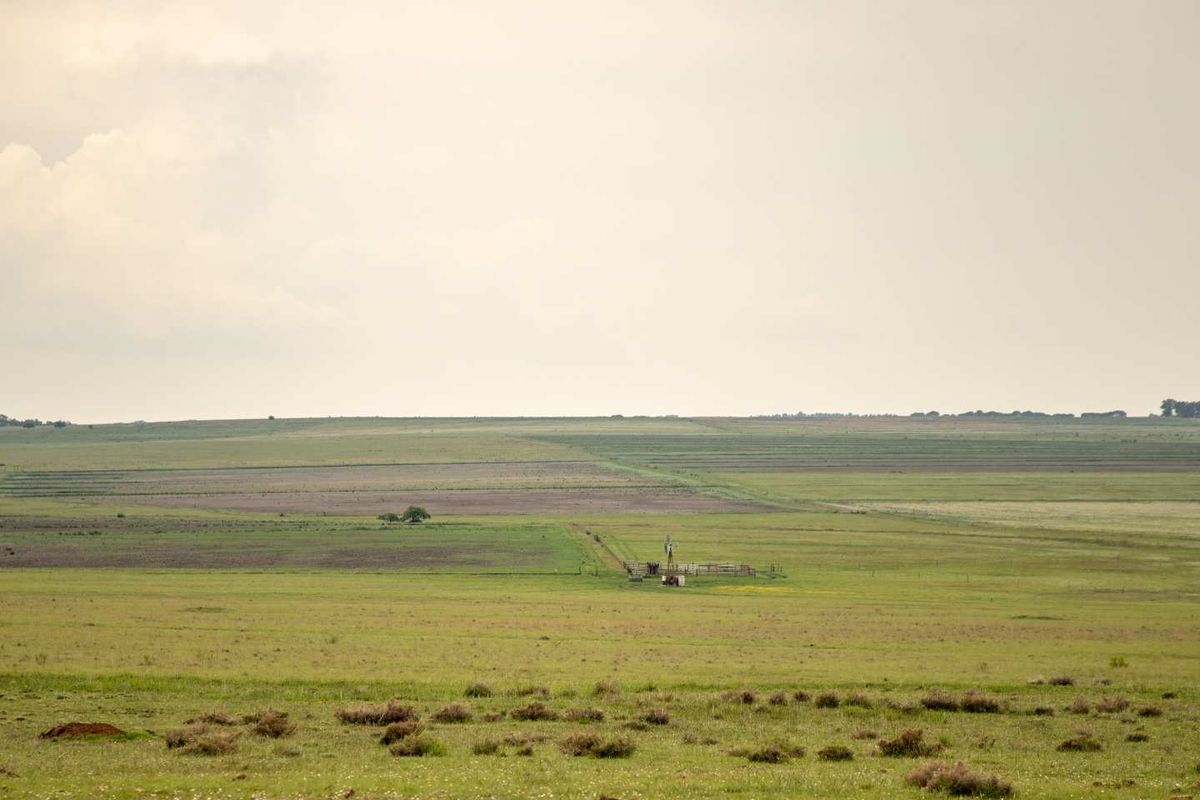 Expansive view of open farm land featuring a traditional wind pump and perimeter fencing across the rolling landscape.
