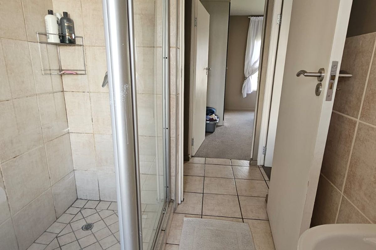 A functional bathroom featuring a glass-enclosed shower with tiled walls and flooring, leading into a carpeted hallway area.