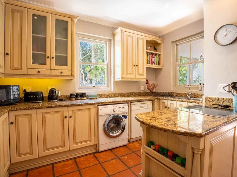 A functional kitchen featuring granite countertops, ample cabinetry, integrated appliances including a washing machine and dishwasher, and classic terracotta-style floor tiles.