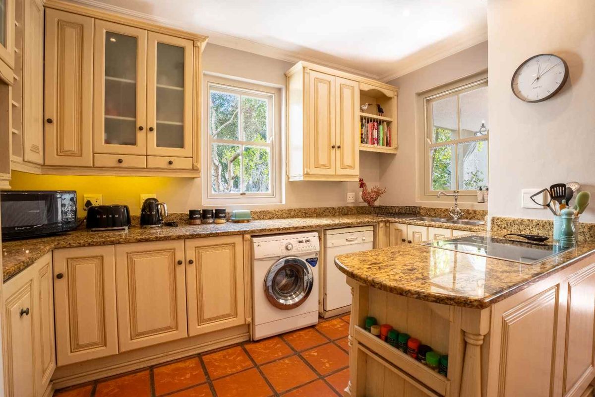 A functional kitchen featuring granite countertops, ample cabinetry, integrated appliances including a washing machine and dishwasher, and classic terracotta-style floor tiles.