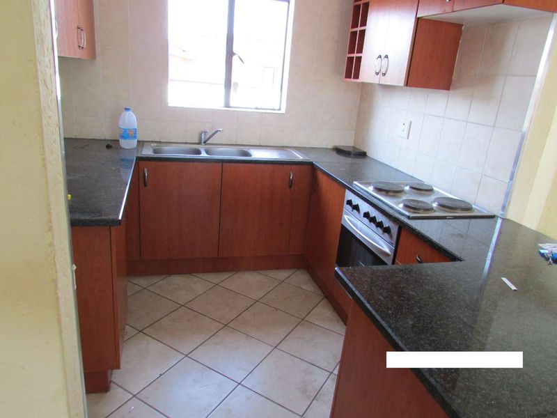 A functional kitchen featuring dark granite countertops, wood-finish cabinetry, a built-in oven with electric hob, and tiled flooring.