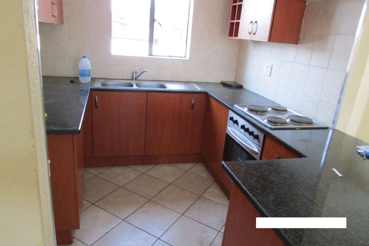 A functional kitchen featuring dark granite countertops, wood-finish cabinetry, a built-in oven with electric hob, and tiled flooring.