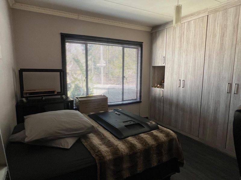 A bedroom featuring extensive built-in wooden cupboards, venetian blinds, and decorative coving, offering practical storage and a neutral foundation.