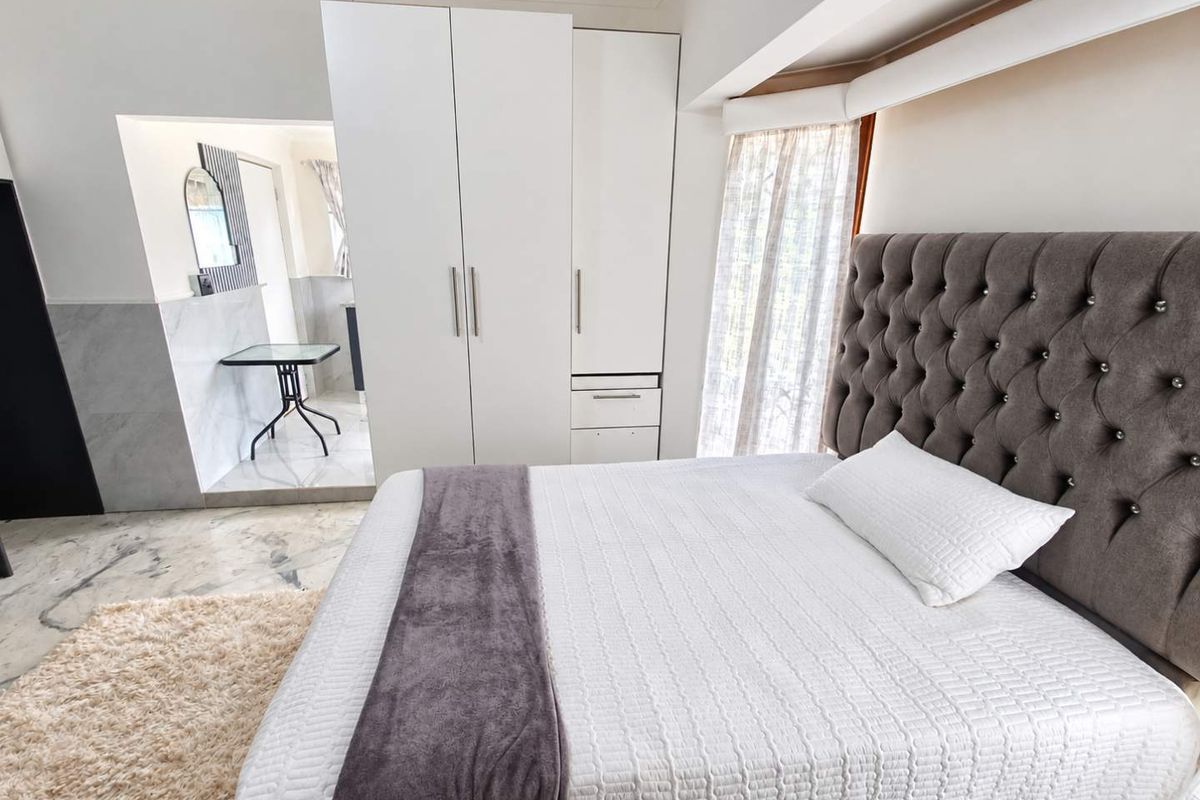 A well-maintained bedroom featuring marble flooring, built-in wardrobes, and a modern tufted headboard, offering a clean and comfortable living space.