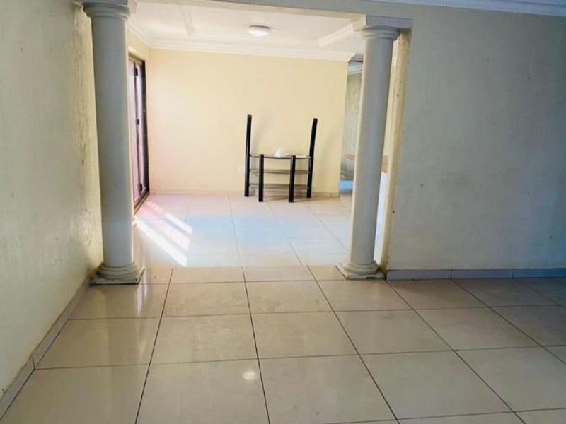 An empty living area featuring tiled flooring, decorative columns, and a sliding glass door leading to the exterior.