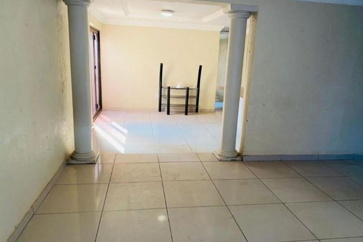 An empty living area featuring tiled flooring, decorative columns, and a sliding glass door leading to the exterior.