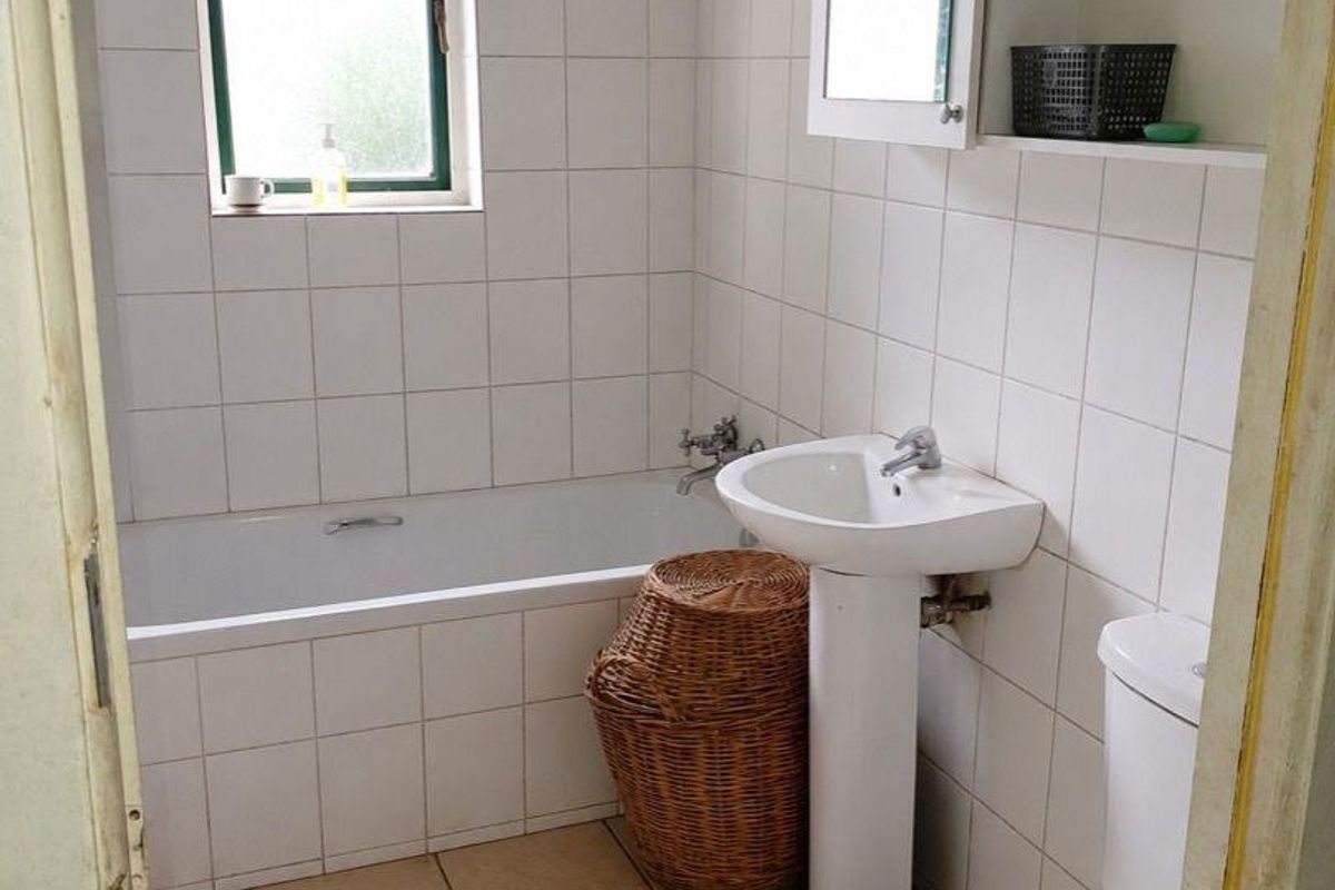 A functional bathroom featuring a bathtub, pedestal basin, toilet, and wall-mounted storage, finished with white wall tiles and neutral floor tiles.
