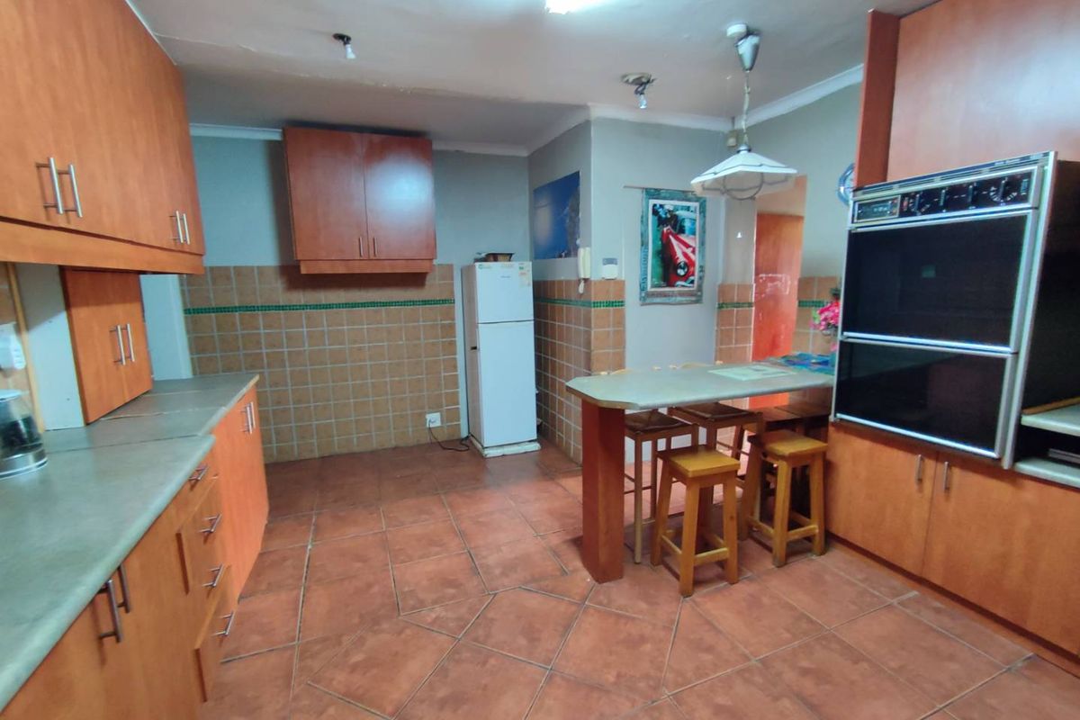 A dated kitchen featuring wood-finish cabinetry, integrated double wall oven, tiled flooring, and a built-in breakfast bar area.