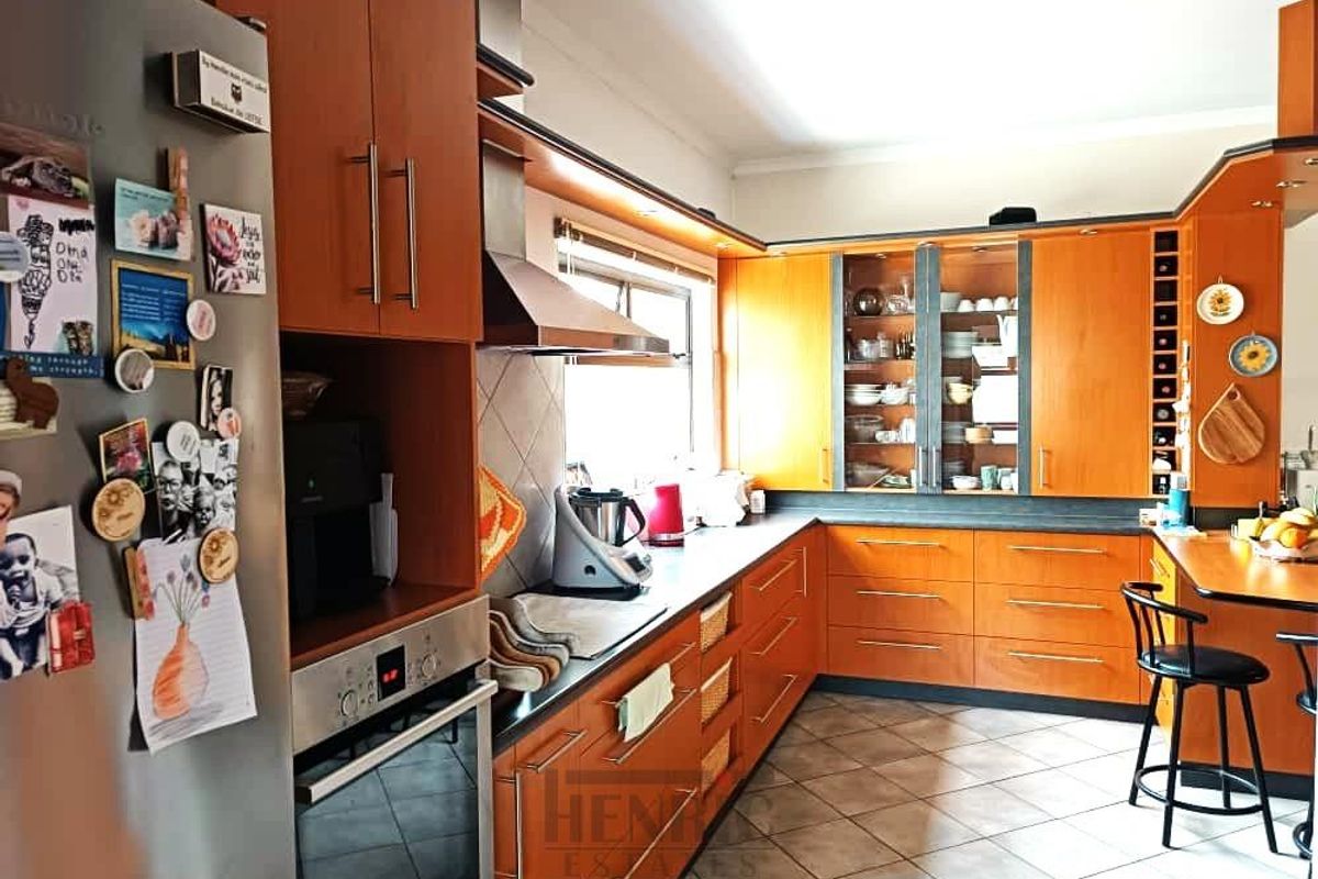 A functional kitchen featuring warm-toned wooden cabinetry, dark countertops, a built-in oven, stainless steel extractor fan, and tiled flooring.