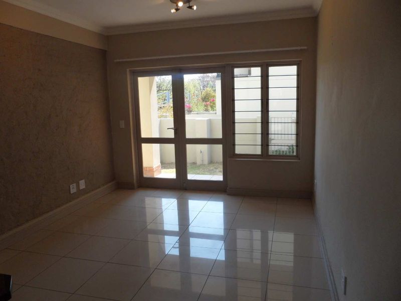 An empty living room featuring polished tiled flooring, a textured accent wall, and glass doors providing access to an outdoor area.
