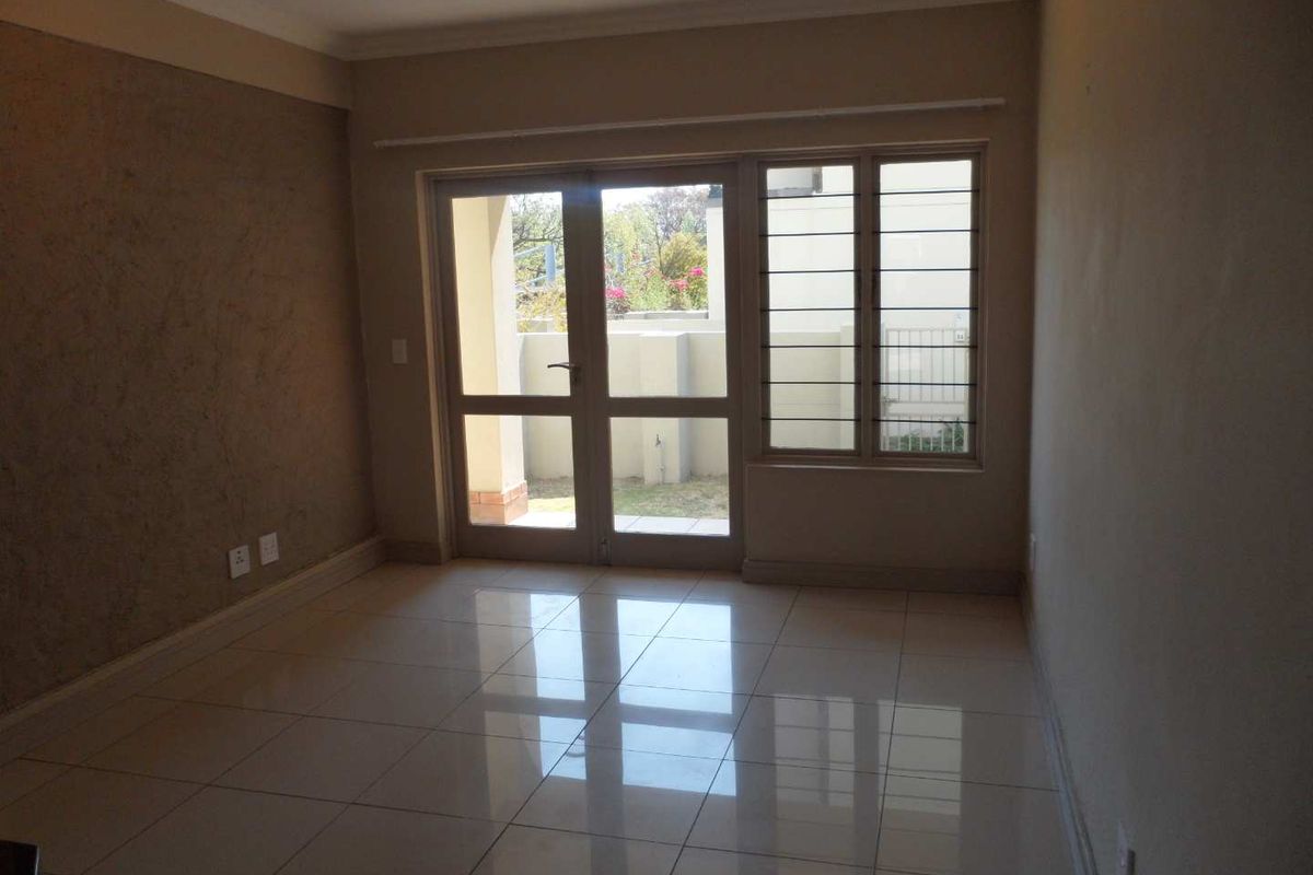 An empty living room featuring polished tiled flooring, a textured accent wall, and glass doors providing access to an outdoor area.