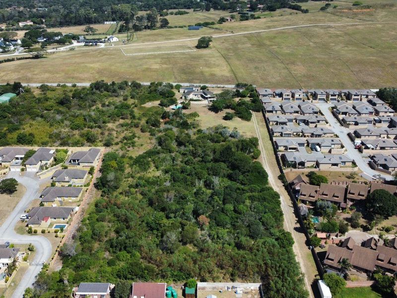 Aerial view of a vacant residential plot surrounded by established housing developments and natural vegetation.