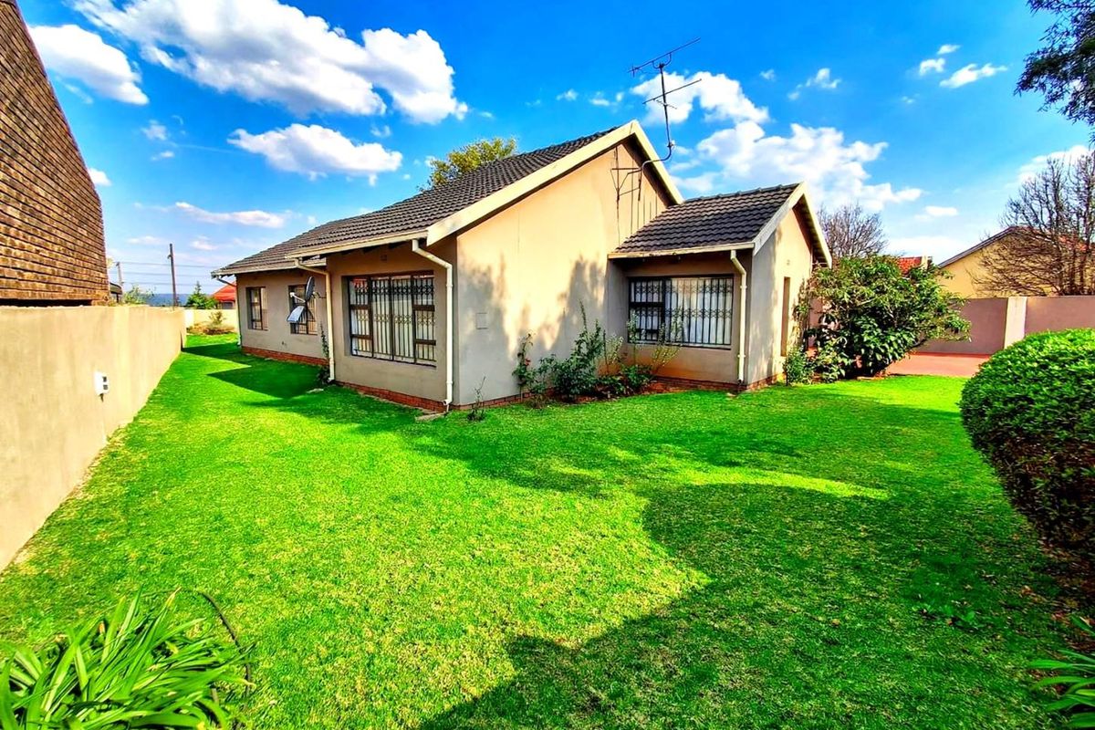 Rear view of the house featuring a tiled roof, security bars on windows, and a well-maintained lawn area.