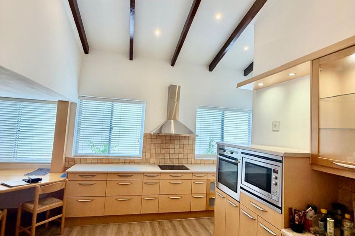 Spacious kitchen featuring light wood cabinetry, built-in double ovens, a stainless steel extractor fan, and vaulted ceilings with exposed timber beams.