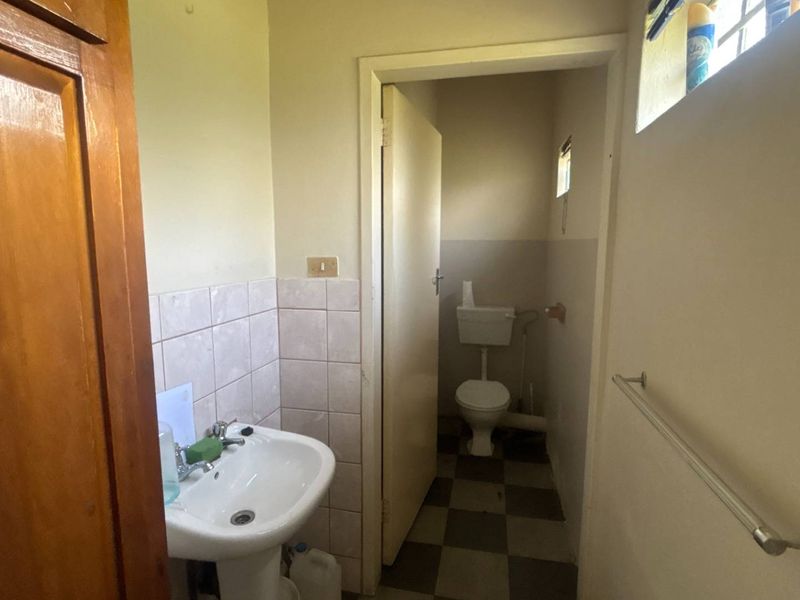 A functional bathroom featuring a pedestal washbasin and a separate toilet area with tiled flooring and walls, requiring cosmetic updates.