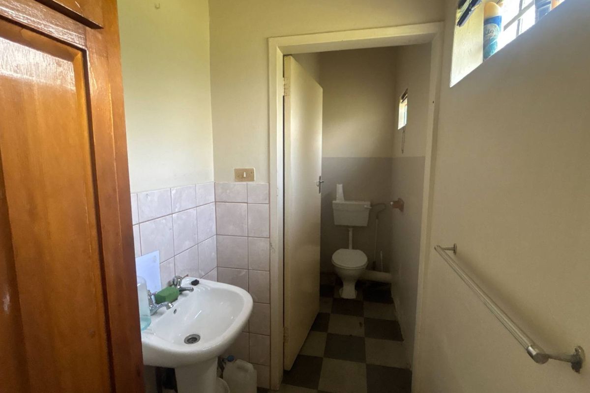 A functional bathroom featuring a pedestal washbasin and a separate toilet area with tiled flooring and walls, requiring cosmetic updates.
