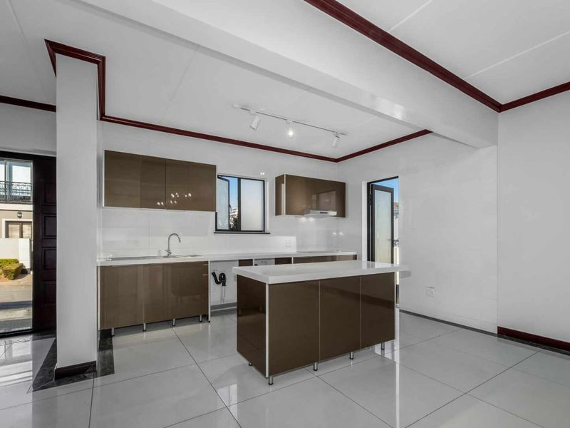 Modern kitchen featuring glossy brown cabinetry, a central island with stone countertops, tiled flooring, and track lighting in an open-plan layout.