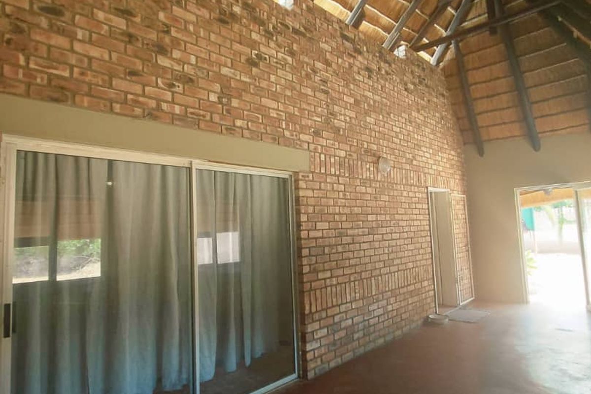 Spacious living area featuring a high vaulted thatched roof with exposed timber trusses and a prominent face-brick feature wall with sliding glass doors.