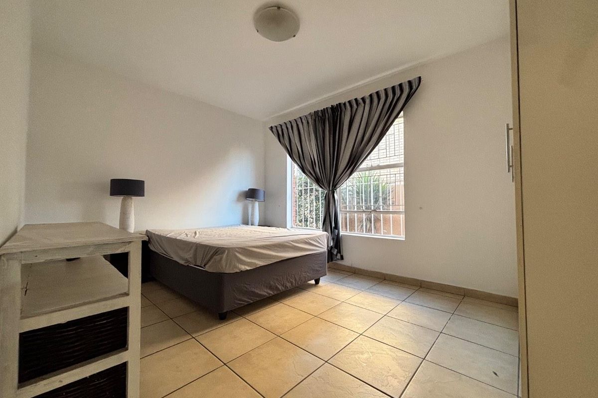 A functional bedroom featuring tiled flooring, a built-in cupboard, and a window fitted with security bars.