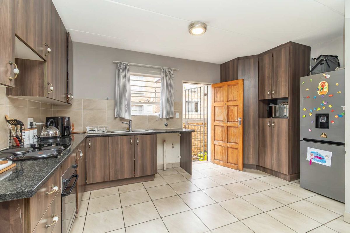 Functional kitchen featuring dark wood-look cabinetry, granite countertops, integrated oven and hob, tiled flooring, and direct access to an exterior area.