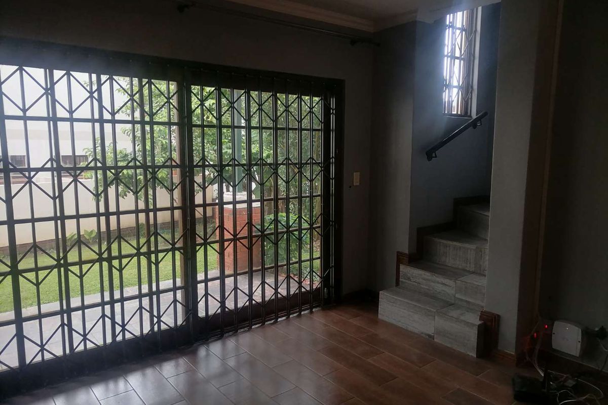 Living area featuring tiled flooring, a staircase with a handrail, and large sliding doors secured with metal security gates leading to the garden.