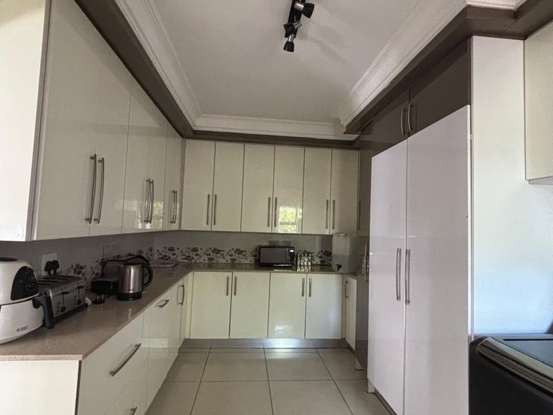 A well-maintained kitchen featuring modern high-gloss cabinetry, tiled flooring, and integrated storage solutions with clean, neutral finishes.