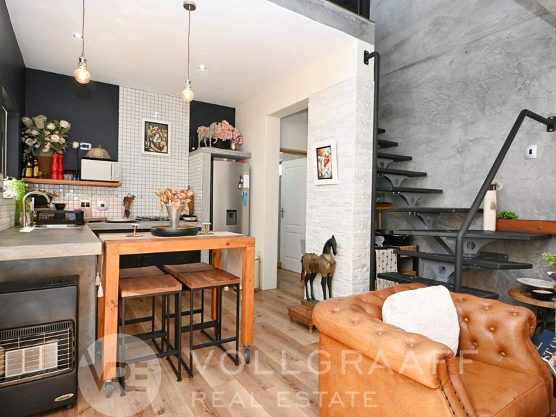 Modern open-plan kitchen and living area featuring industrial-style concrete finishes, a sleek staircase, and contemporary tiled backsplash.