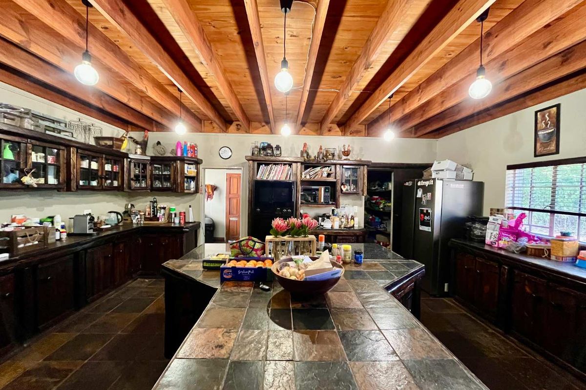Spacious farmhouse kitchen featuring exposed timber beam ceilings, dark stone-tiled island countertop, and extensive custom wooden cabinetry with integrated storage solutions.