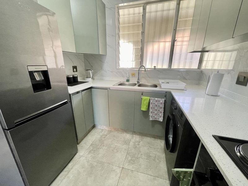 A modern, well-maintained kitchen featuring sleek cabinetry, quartz countertops, a double sink, and integrated laundry facilities with tiled flooring and louvered windows.